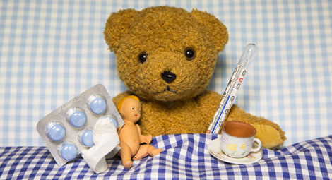 a teddy bear tucked up in bed with tablets and a thermometer