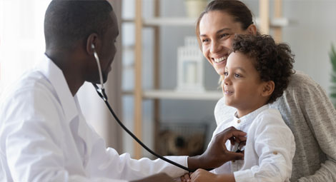 Doctor using a stethoscope on a little boy who is being held by his mother